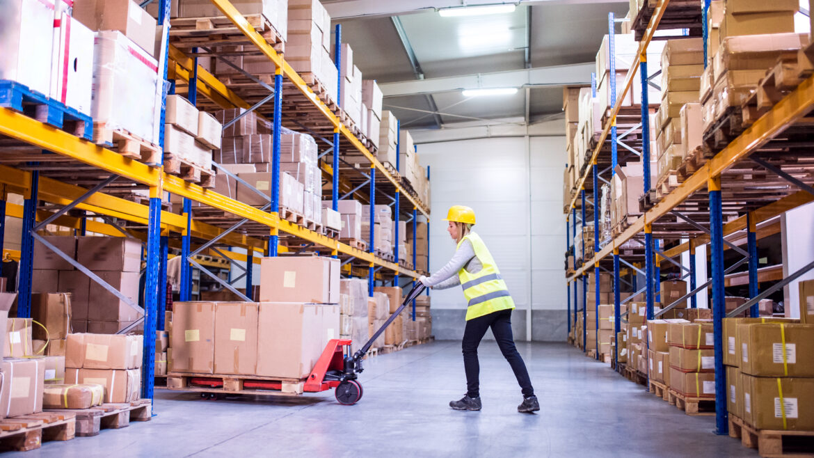 Young woman warehouse worker with hand forklift truck.